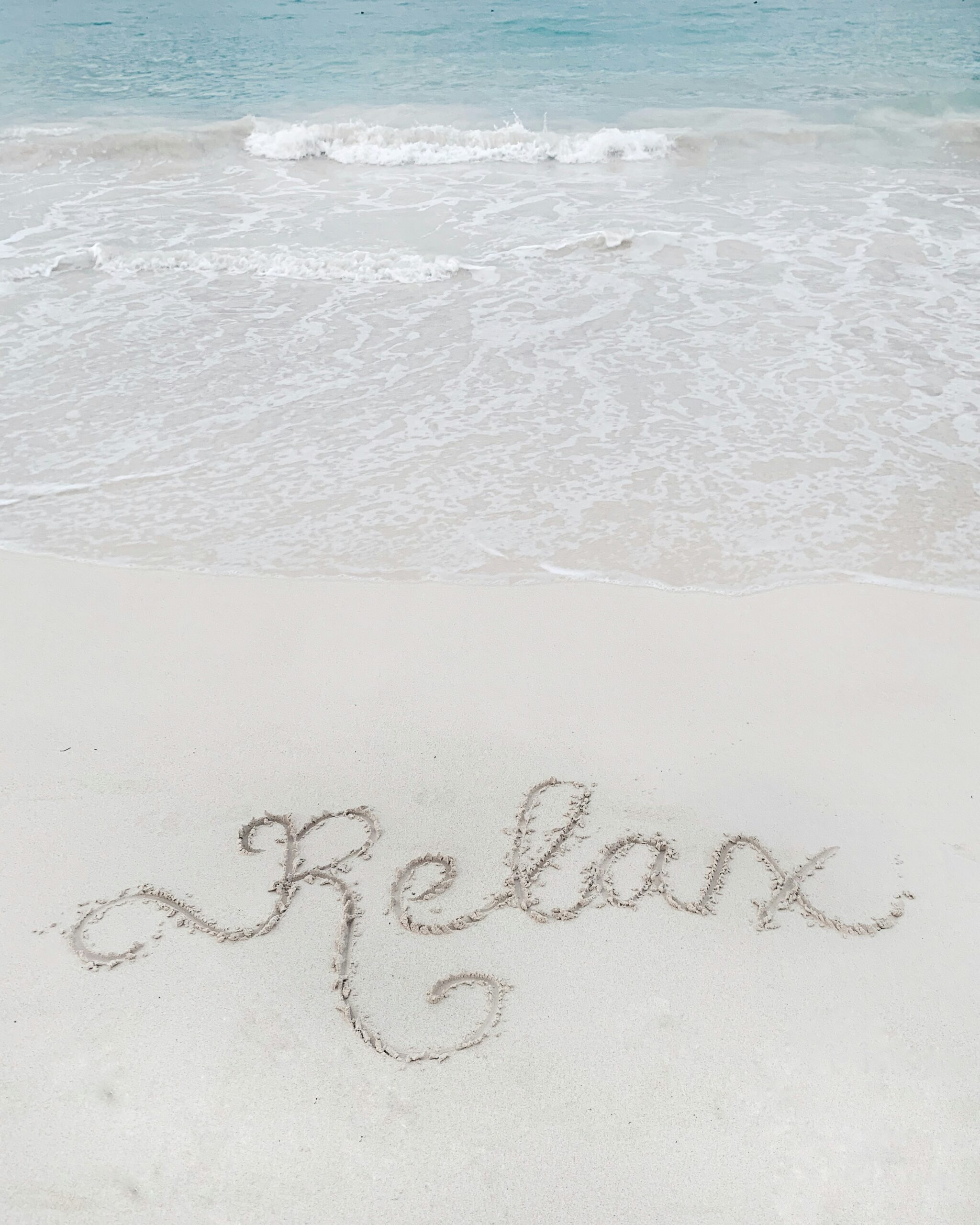 "Relax" skrivet i sanden på stranden.
